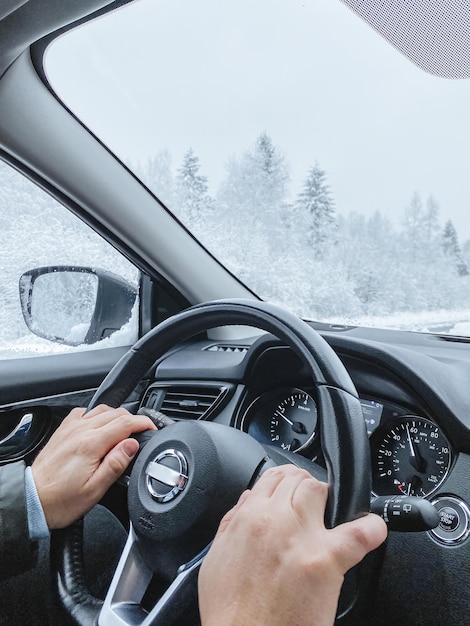 Handen van een mannetje op het stuur van een auto besneeuwd landschap buiten het raam van de auto