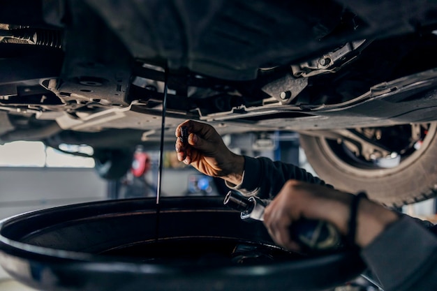 Handen van een monteur die de olie uit de motor laat lopen in de mechanic39s-winkel