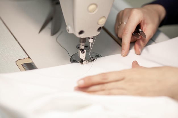 Handen van een naaister die kleding naait van witte stof op een naaimachine-closeup