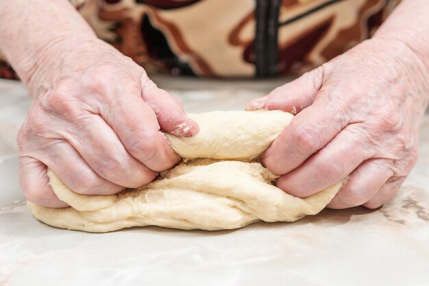 Handen van een oudere vrouw kneden het deeg op een tafel, close-up