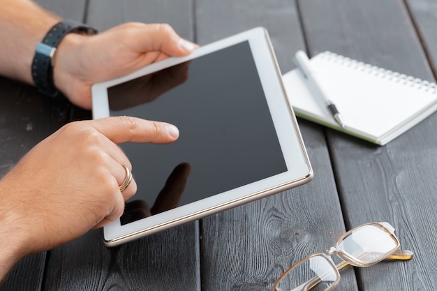 Handen van een tablet-apparaat van de mensenholding over een houten werkruimtelijst