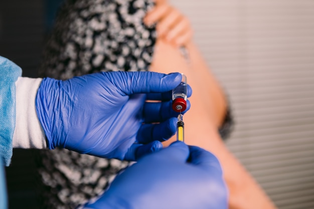 Handen van een verpleegster vullen de spuit met het vaccin uit de injectieflacon om een oudere vrouw een vaccin in de arm te injecteren