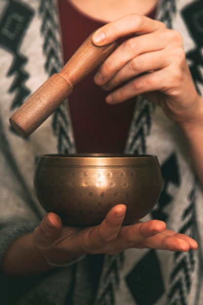 Handen van een vrouw die een tibetaanse kom gebruikt, gekleed met handgemaakte poncho kopieerruimte meditatie verticaal