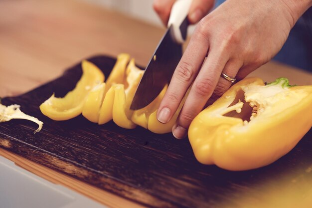 Foto handen van een vrouw die paprika op houten scherpe raad snijdt