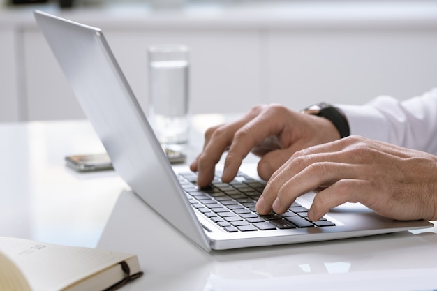 Handen van hedendaagse zakenman of ondernemer toetsen van laptop toetsenbord aan te raken tijdens het werken met online gegevens