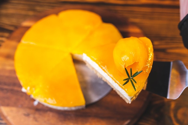 Handen van jonge chef-kok die een plakje mango cheesecake snijdt