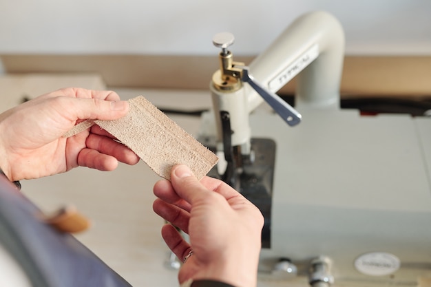 Handen van jonge creatieve vakman met klein stukje blond suède door elektrische machine tijdens het werkproces