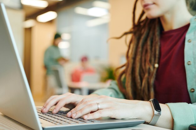 Handen van jonge hedendaagse vrouwelijke officemanager in vrijetijdskleding over laptoptoetsenbord tijdens presentatie van presentatie door haar werkplek