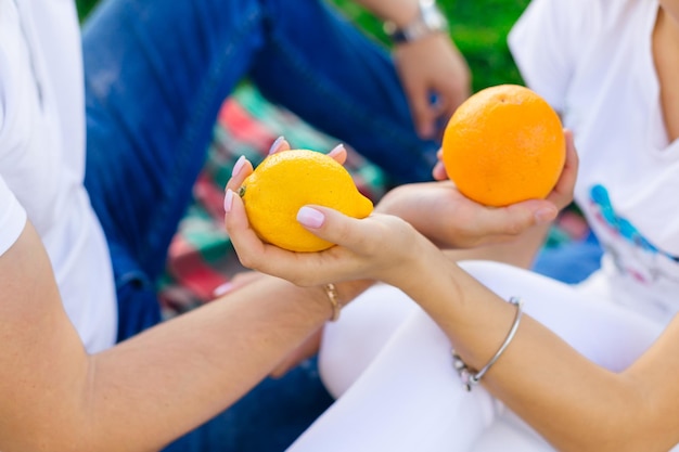 handen van jonge mensen die heerlijke sinaasappels uitwisselen terwijl ze op dekens in de natuur zitten
