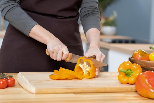 Handen van jonge vrouw die verse gele paprika hakt