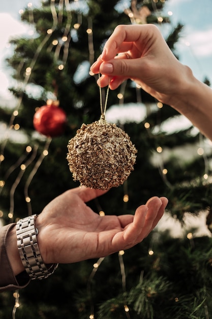 Handen van jonge vrouw gouden versieren kerst speelgoed bal geven aan haar man om ze op de kerstboom te zetten voor de viering