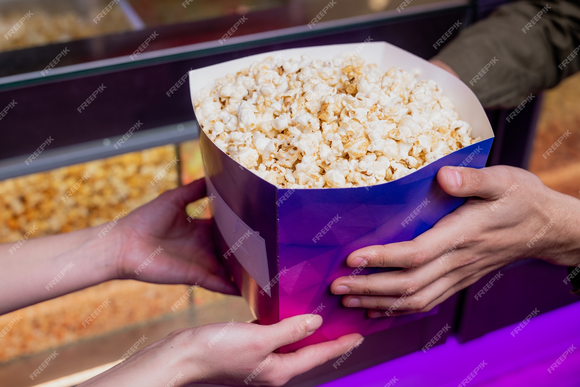 Handen jonge vrouwelijke verkoper passeren grote paarse kartonnen doos vol popcorn terwijl ze het verkopen aan een van de toeschouwers in bioscoop | Premium Foto