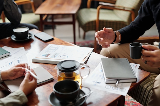 Handen van jonge zakenman met kopje thee in gesprek met collega's