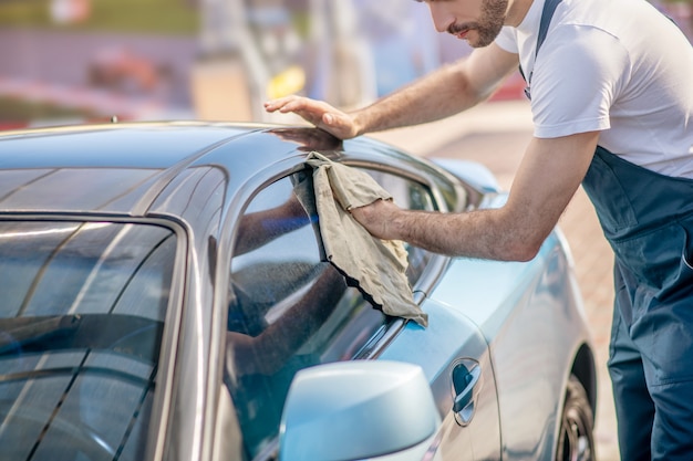 Handen van man die zijruit van auto afvegen