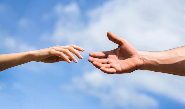 Handen van man en vrouw op blauwe hemelachtergrond Een helpende hand bieden Solidariteit, mededogen en liefdadigheid redden Handen van man en vrouw die naar elkaar reiken ondersteunen Een helpende hand geven