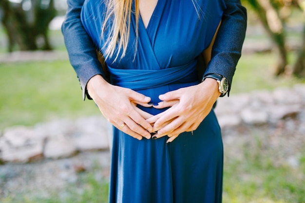 Handen van man knuffel achter zwangere buik van vrouw in een blauwe jurk