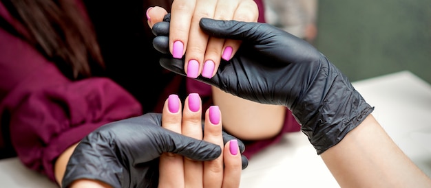 Handen van manicure houden vrouwelijke vingernagels met roze nagellak