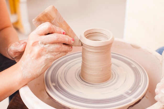 Handen van meisje dat aardewerk maakt van witte klei op een pottenbakkersschijf