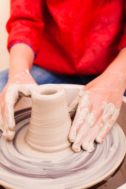 Handen van meisje dat aardewerk probeert te maken van witte klei op een pottenbakkersschijf