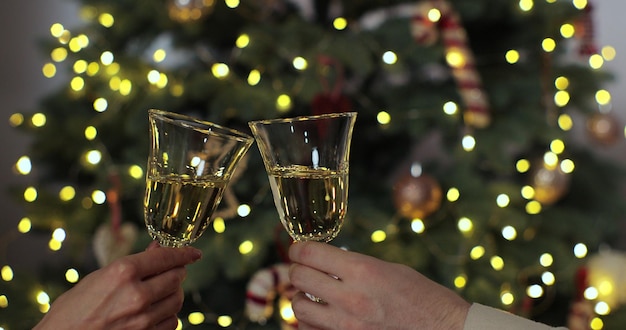 Handen van mensen die juichen met glazen champagne tegen kerstboom versierd met gloeiende guirlande Wintervakantie festival stemming toast