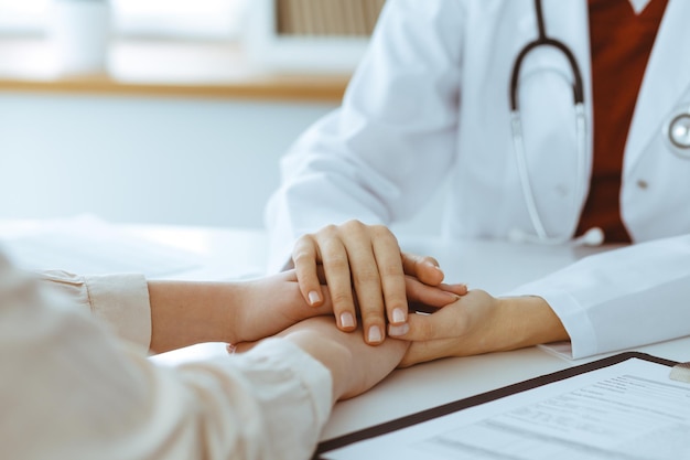 Handen van onbekende vrouw-dokter die haar vrouwelijke patiënt, close-up geruststelt. geneeskunde concept.