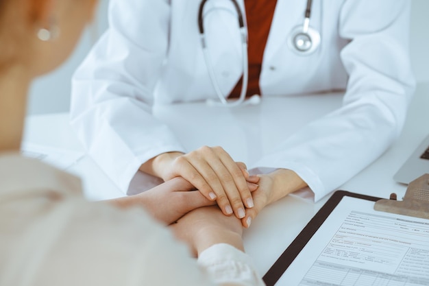 Handen van onbekende vrouw-dokter die haar vrouwelijke patiënt, close-up geruststelt. Geneeskunde concept.