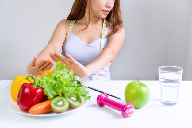 Handen van ongelukkige aziatische vrouw duwen groenten en fruit met verveelde emotie op een dieet