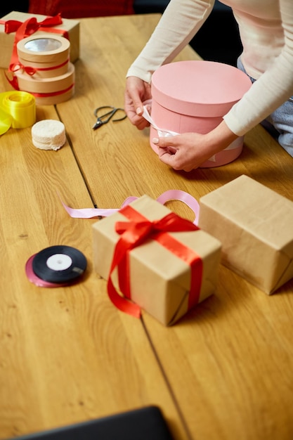 Handen van onherkenbare vrouw die met lint een roze cadeau verpakt