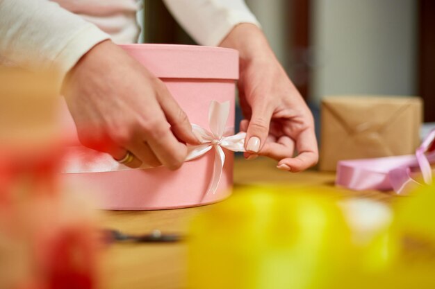 Handen van onherkenbare vrouw die met lint een roze cadeau verpakt