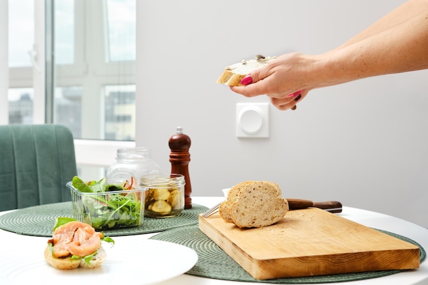 Handen van onherkenbare vrouw die roomkaas op sandwich uitspreidt