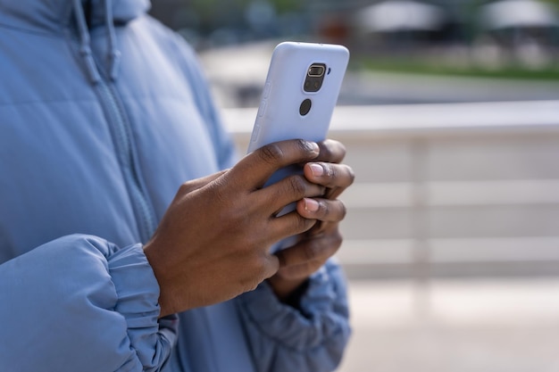 Handen van onherkenbare zwarte etnische man met telefoon en blauwe jas in de stad