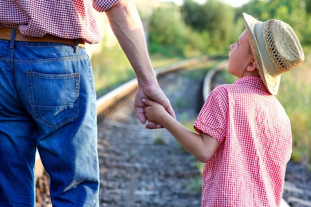 Handen van ouder en zoon in cowboyhoed bij de spoorweg met koffer