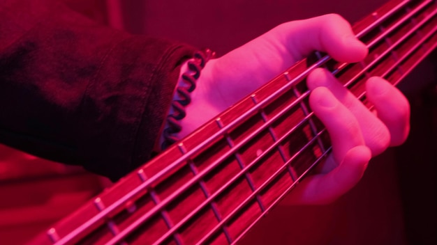 Handen van rockmuzikant die de elektrische basgitaar speelt bij herhaling in rood licht