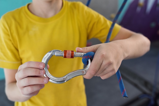 Handen van schooljongen in geel t-shirt met karabijnhaak aan touw klimmen terwijl hij training in de sportschool gaat hebben