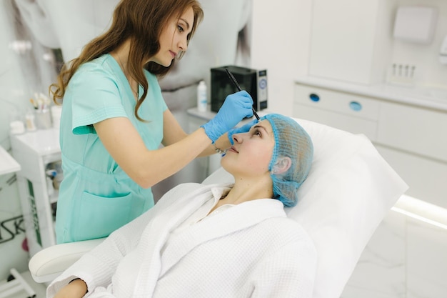 Handen van schoonheidsspecialist die voorbereidingen treffen voor gezichtscontouring plastiek Jonge vrouw krijgt gezichtsbehandeling