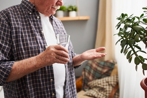 Handen van senior man met glas water en pil