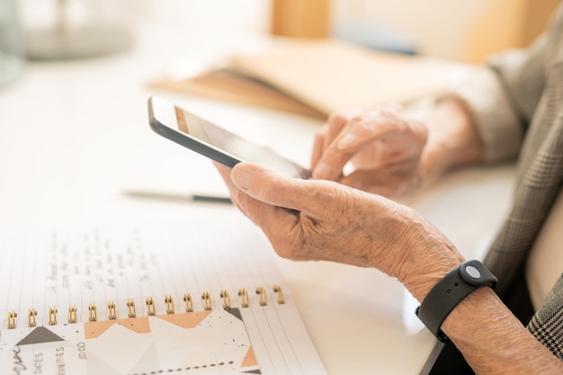 Handen van senior mobiele vrouw met smartphone over notitieblok openen met notities hen te fotograferen