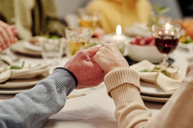 Handen van senior paar bidden door geserveerd feestelijke tafel