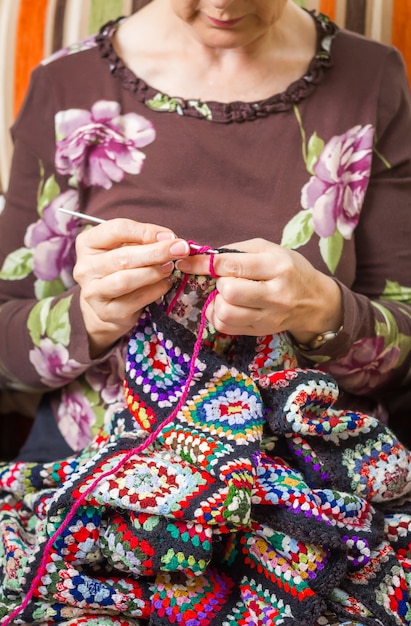 Handen van senior vrouw die een vintage wollen quilt breit met kleurrijke patches