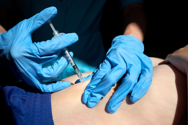 Handen van verpleegster in blauwe chirurgische handschoenen die injectie van antistollingsmiddel subcutaan aan kind maken.