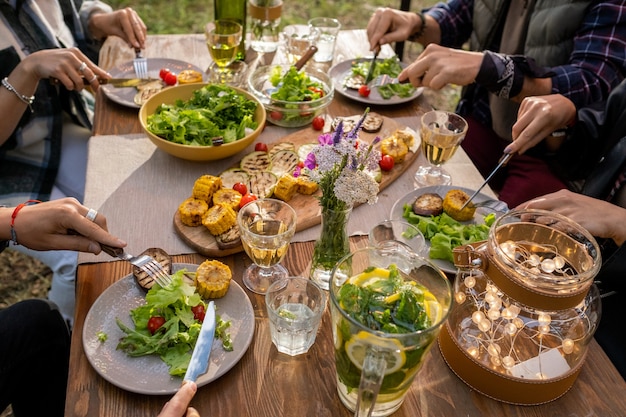 Handen van verschillende vrienden die met messen en vorken groenten eten