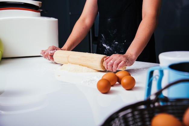 Handen van vrouw die deeg maken met houten rollen