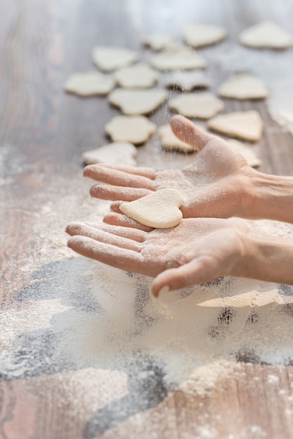 Handen van vrouw die één van ruwe koekjes in vorm van hart houden terwijl het koken van eigengemaakt gebakje