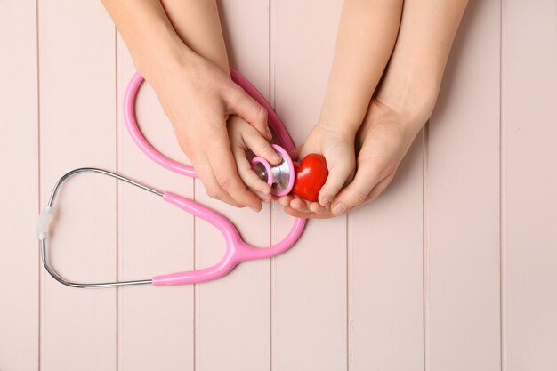 Handen van vrouw en kind met rood hart en stethoscoop op houten.