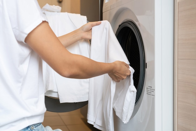 Handen van vrouw laden witte kleur kleding in wasmachine in keuken thuis. wasconcept.