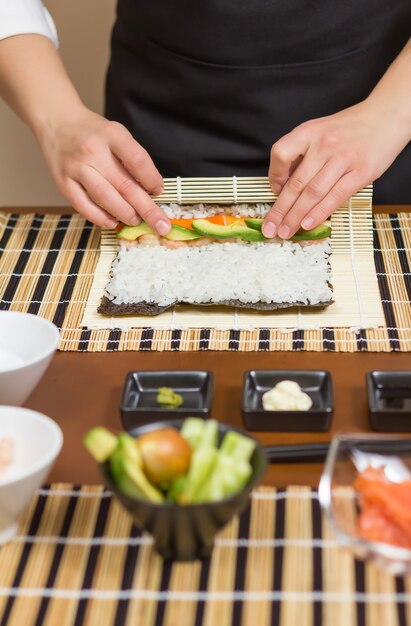 Handen van vrouwelijke chef-kok die een Japanse sushi oprollen