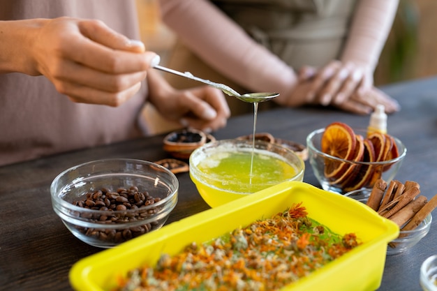 Handen van vrouwen die gesmolten zeepmassa in siliconencontainer met droge natuurlijke ingrediënten gieten terwijl ze thuis cosmetisch product maken