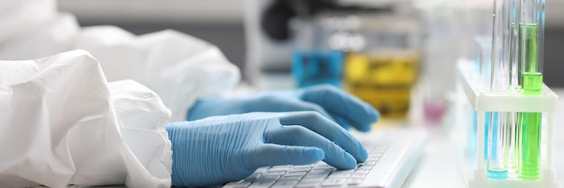 Handen van wetenschapper in handschoenen werken op toetsenbord in wetenschappelijk laboratoriumonderzoek en gegevens