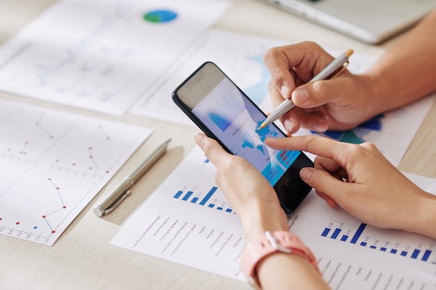 Handen van zakenmensen die een smartphone met kaart op het scherm aanwijzen bij het controleren van online verkoopgegevens