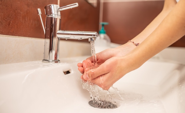 Handen wassen met water en vloeibare zeep in de badkamer.